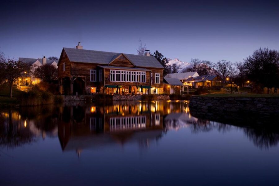 Cozy lakeside mountain lodge at dusk reflecting on calm water in a tranquil resort setting.