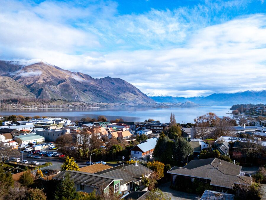Scenic Wanaka lakeside town with snowy alpine mountains, calm blue lake, and cloudy sky.