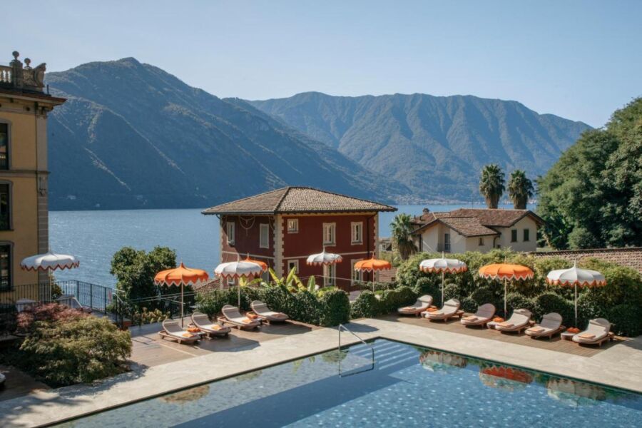 Luxurious lakeside resort with pool, loungers, villas, and picturesque mountain backdrop.