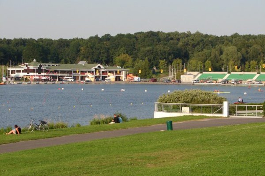 Poznań Malta Lake waterfront park with rowing boats, boathouse, spectator stands, trees.