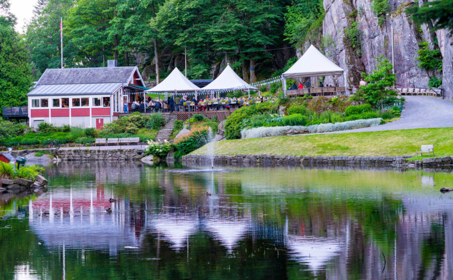 Lakeside cafe with white festival tents, red boathouse, and pond reflections.