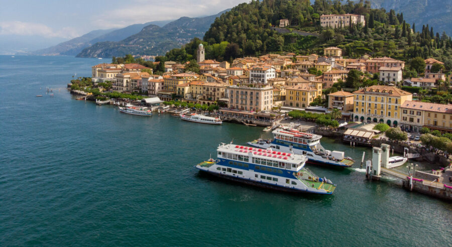 Lake Como ferry and harbor with terracotta-roofed Italian lakeside town and bell tower.