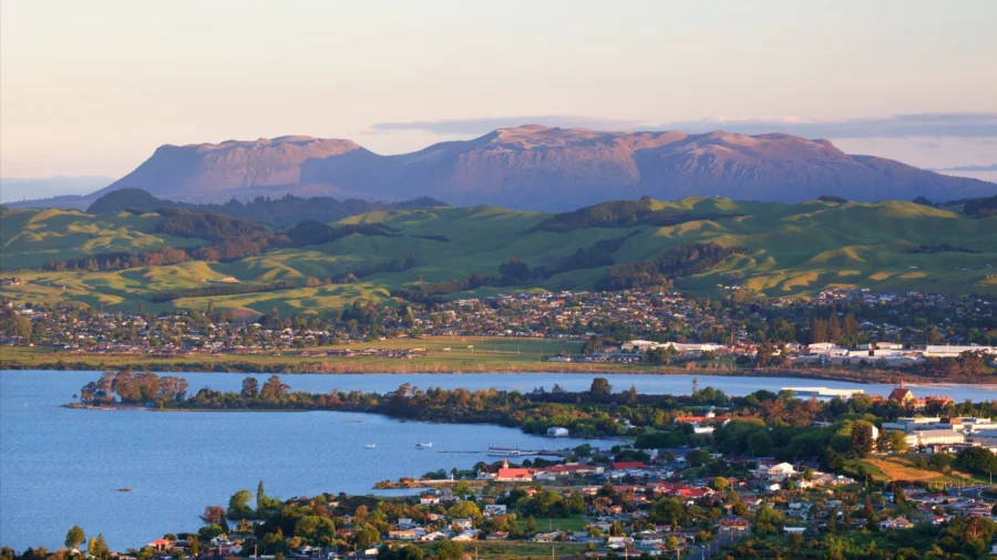 Panoramic lakeside town with calm water, green hills, and flat-topped mountain range at sunset.