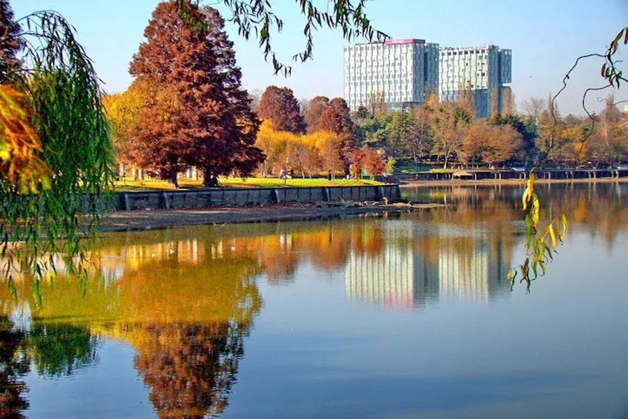 Tranquil lake with autumn foliage and modern building in Herastrau Park.