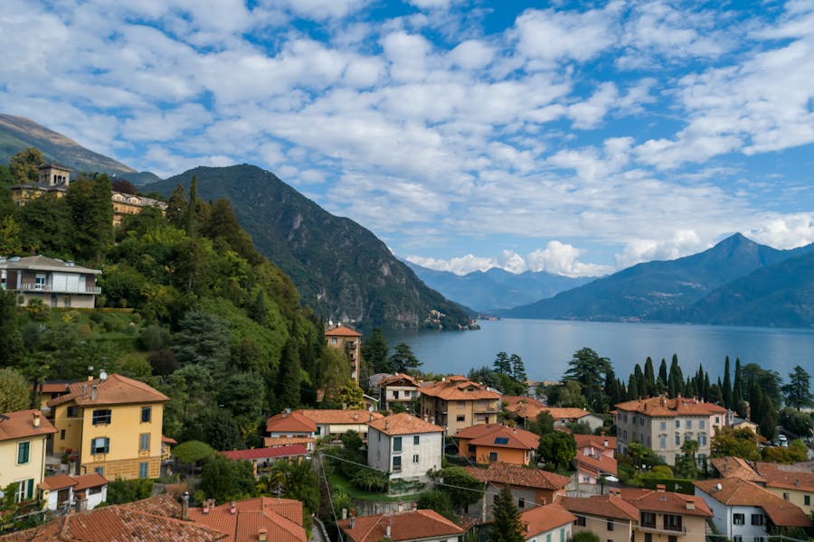 Lake Como, Italy lakeside village with red-tiled roofs on a forested hillside by calm lake.
