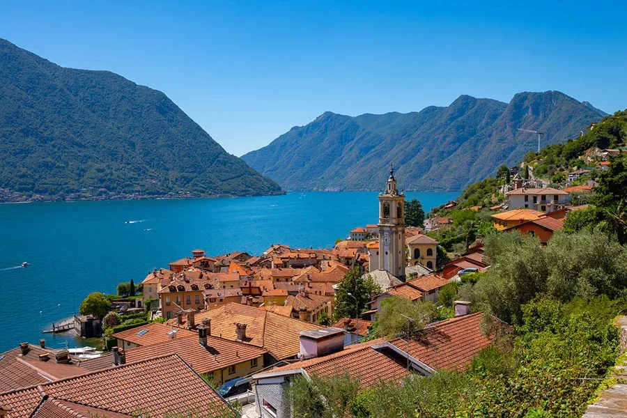 Lake Como lakeside village with terracotta roofs, church tower and blue water, Italy.