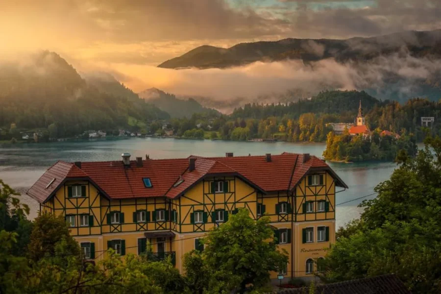 Yellow timber lakeside hotel in Bled, Slovenia with island church and mountain views.