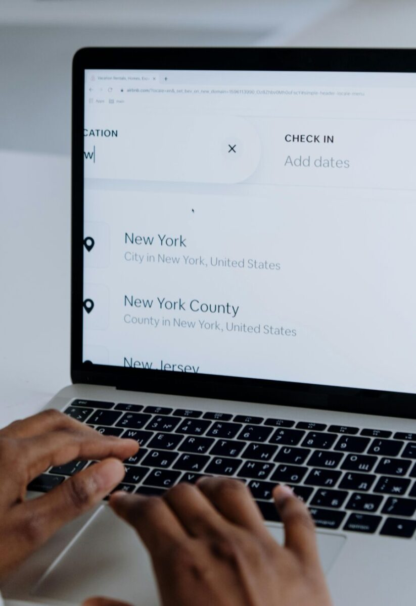 Person typing on laptop doing Airbnb travel search, planning trip locations.