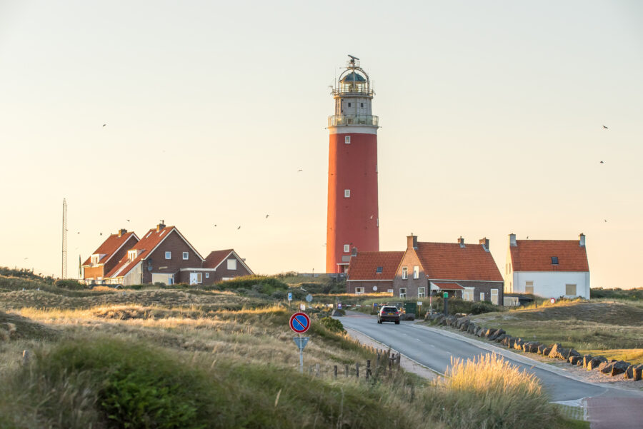 The Leuchttrum Eierland lighthouse in Texel, Netherlands, features a red and white striped tower amidst coastal scenery.