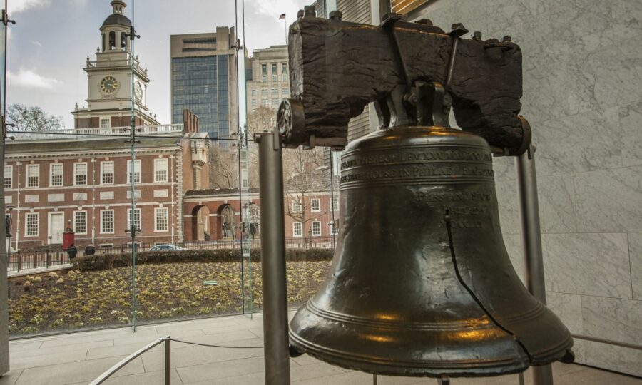 Liberty Bell with crack in glass pavilion, Philadelphia; Independence Hall and skyscrapers in view.