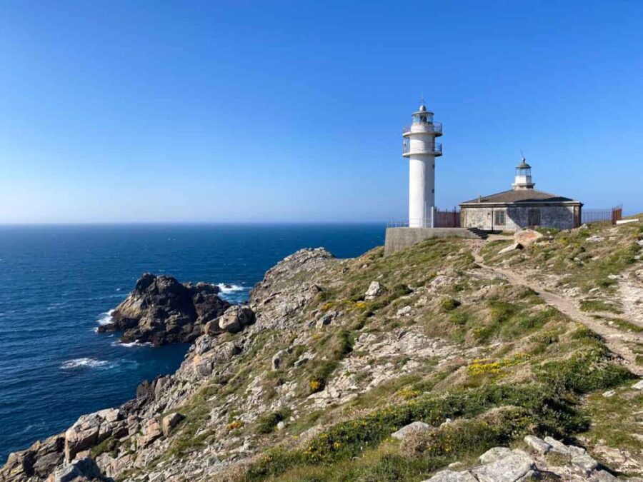 Tourinan lighthouse on rocky cliff overlooking Atlantic coast with coastal path and crashing waves.