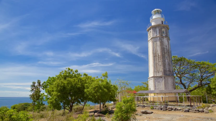 Malapascua Lighthouse on rocky Philippine coast with blue ocean and sky.