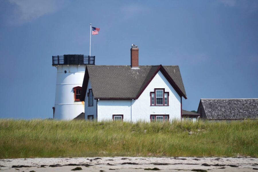 Chatham Coastal lighthouse and seaside home against blue sky with American flag.