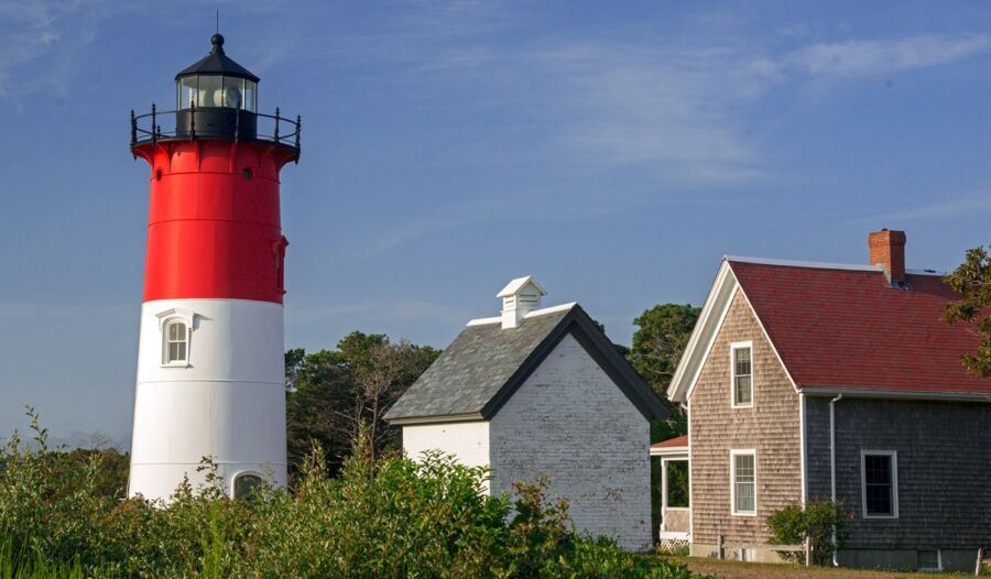 Eastham Vibrant lighthouse with red and white sections beside coastal cottages and greenery.