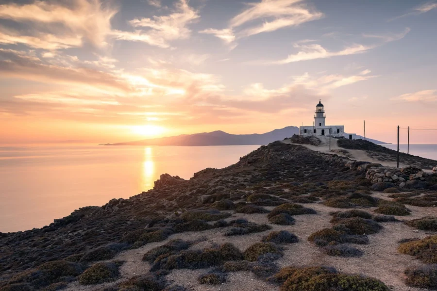 Sunset over rocky coast with lighthouse, ocean reflection, and colorful sky.