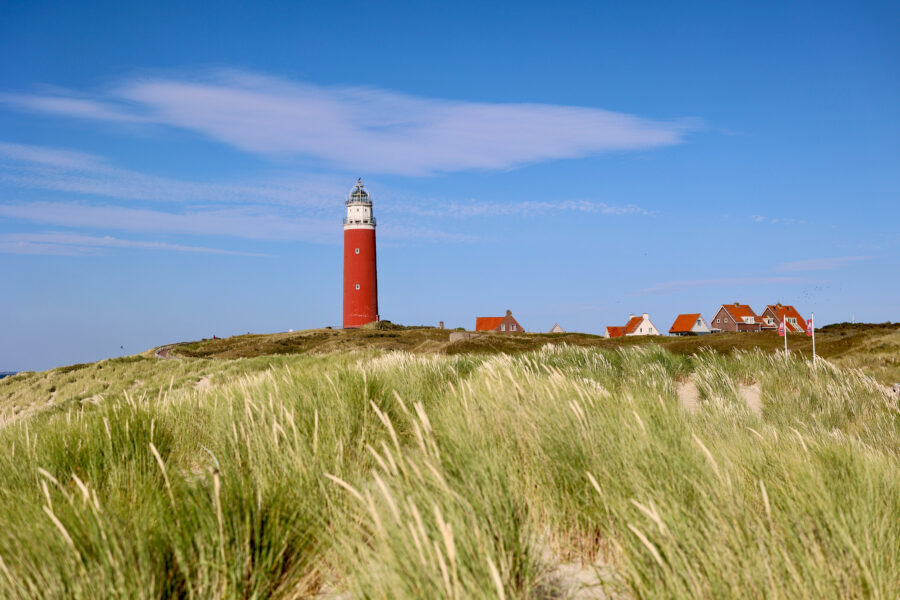 The Texel Island lighthouse in the Netherlands, framed by tall sand dunes and illuminated by warm sunlight.