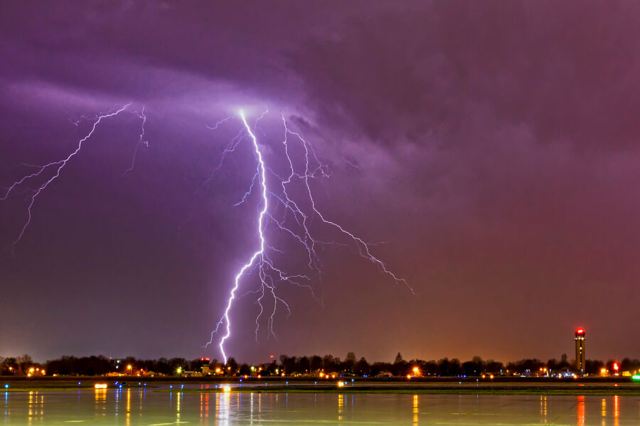 Lightning strikes during a thunderstorm at the airport, casting a bright flash against the sky