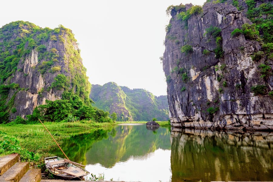 Serene limestone river canyon landscape with cliffs, calm water reflection, lush greenery and wooden boat.