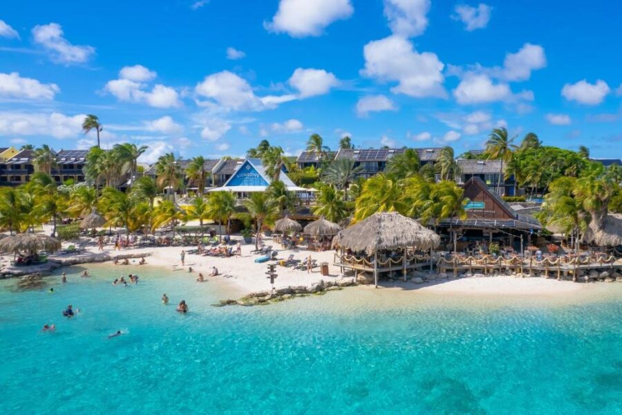 Scenic view of LionsDive Beach Resort's beach, featuring soft sand and clear turquoise waters under a bright blue sky.
