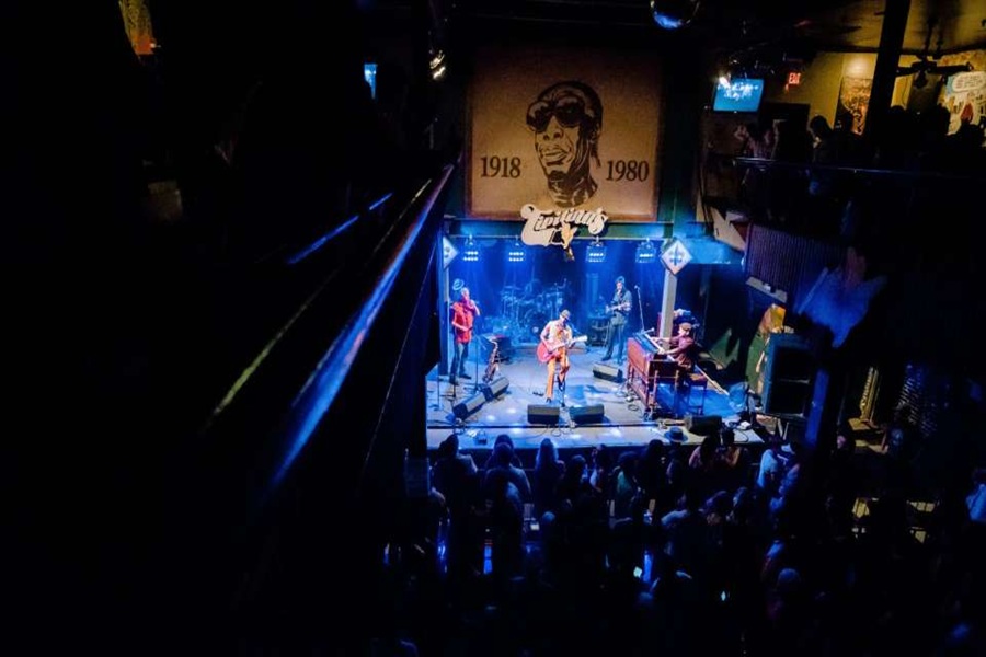 Live music venue with vibrant performance, mural backdrop, and engaged diverse audience.
