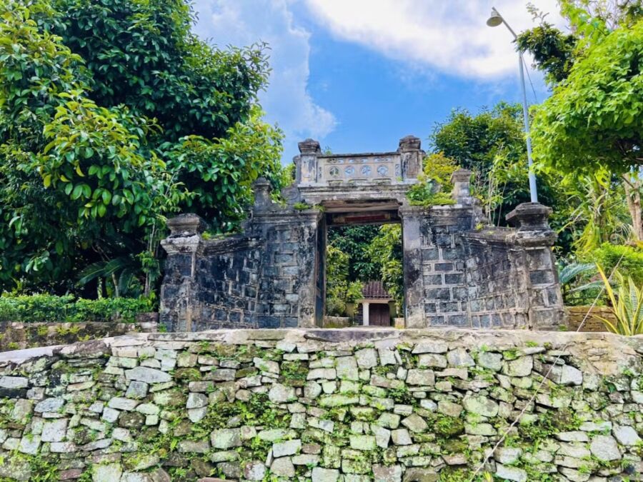 Ancient stone gate surrounded by jungle foliage under a clear blue sky at Lộc Yên Ancient Village, Vietnam.