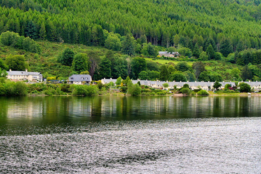 Scenic view of a boat traveling on a river, with a house visible in the background, highlighting Loch Ness, Scotland's beauty.