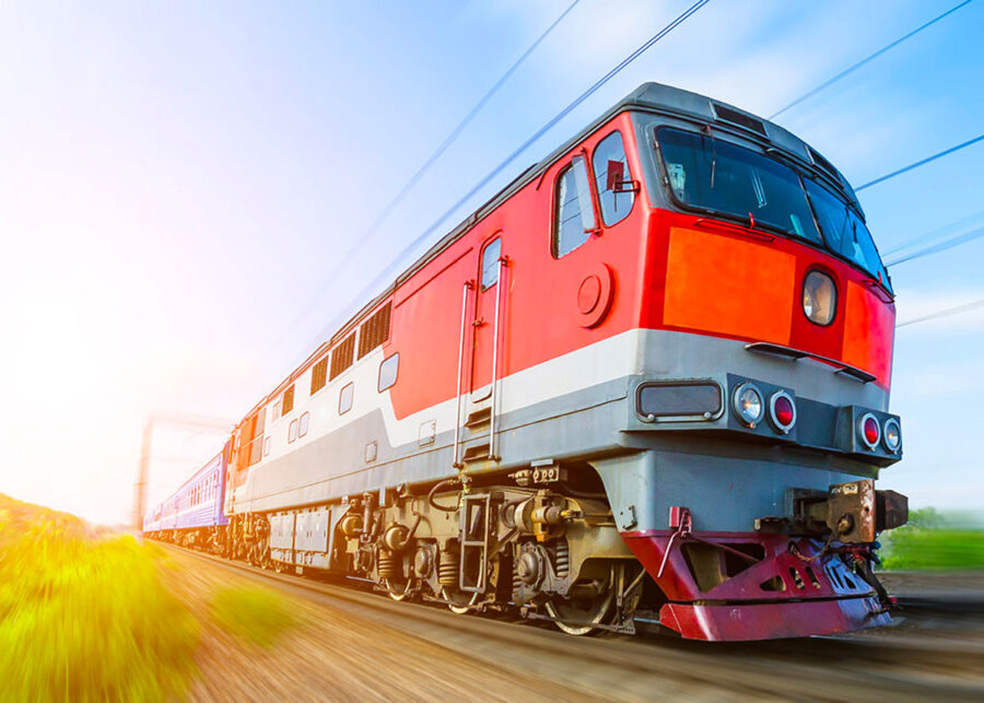 High-speed red and grey train in countryside, illustrating modern rail travel and engineering.