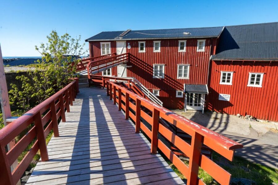 Wooden bridge leads to the red Lofoten Å HI Hostel building surrounded by natural scenery.