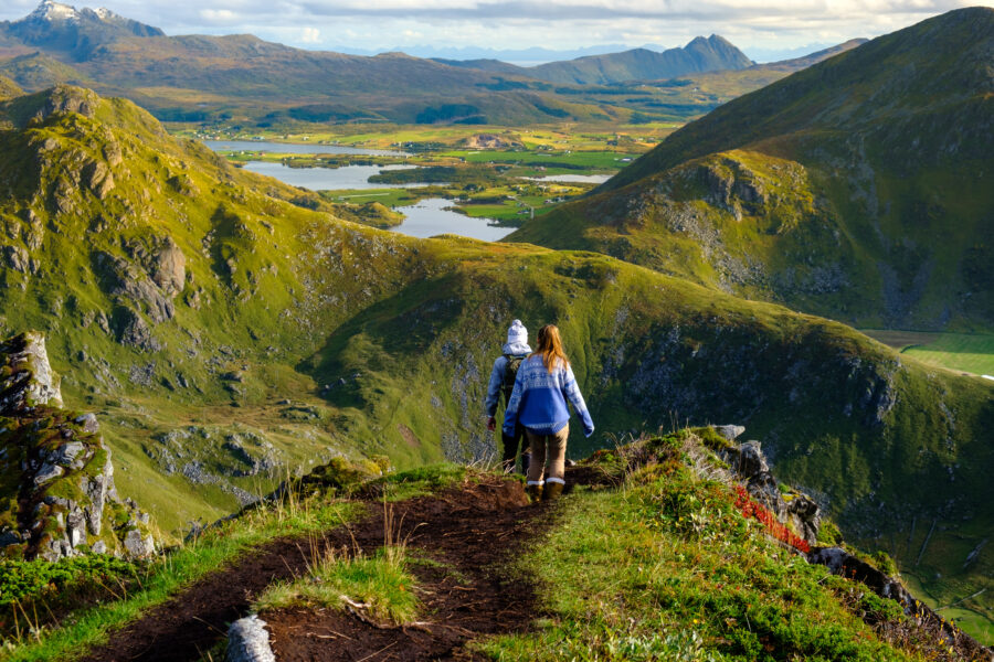 Couple stands atop a mountain range in the Lofoten Islands, surrounded by stunning natural scenery during their trek.
