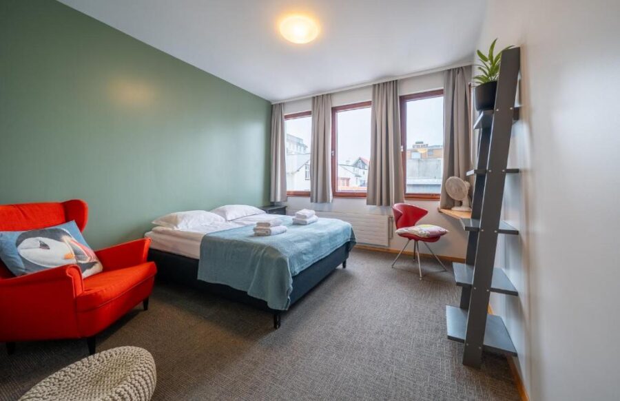 Interior of a bedroom at Loft - HI Eco Hostel, Reykjavik, showcasing a bed, a chair, and a bright window.