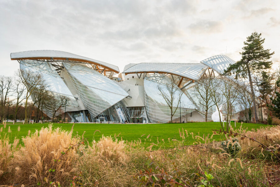Exterior view of the Louis Vuitton Foundation in Paris, showcasing its modern architecture and glass sails against a blue sky.