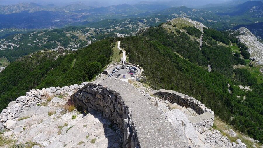 Panoramic view from the summit of Lovćen National Park, showcasing lush mountains and valleys under a clear blue sky.