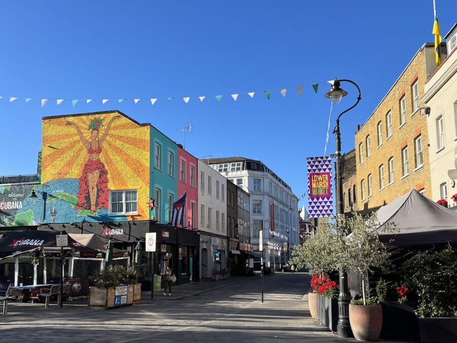 Lower Marsh Market street in London with colorful murals, cafes, planters, and market stalls.