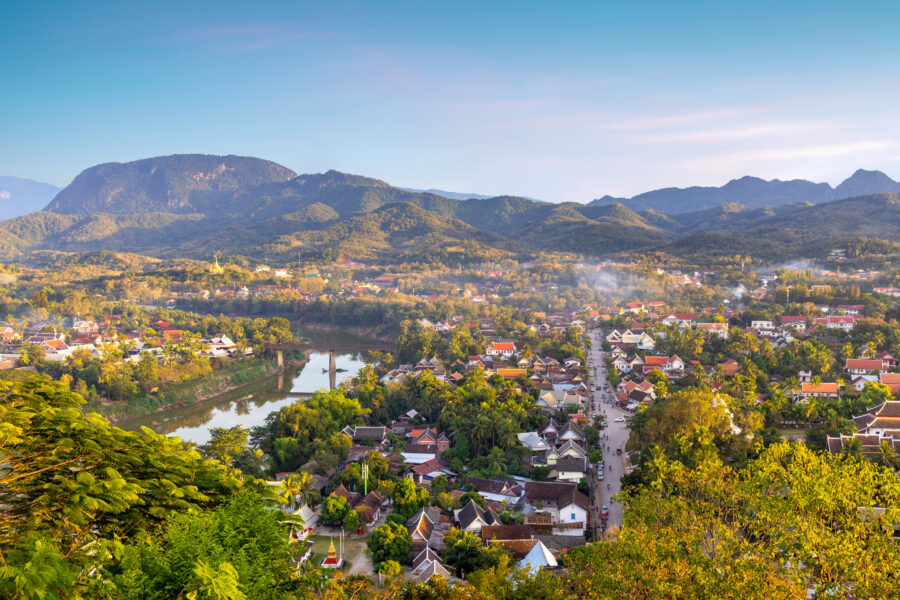 Aerial view of Luang Prabang city at sunset, showcasing vibrant colors and the Mekong River winding through the landscape.