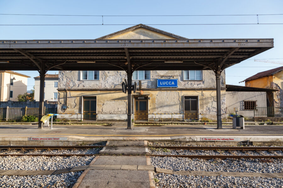 Exterior view of Lucca Train Station in Italy, showcasing its historic architecture and surrounding greenery
