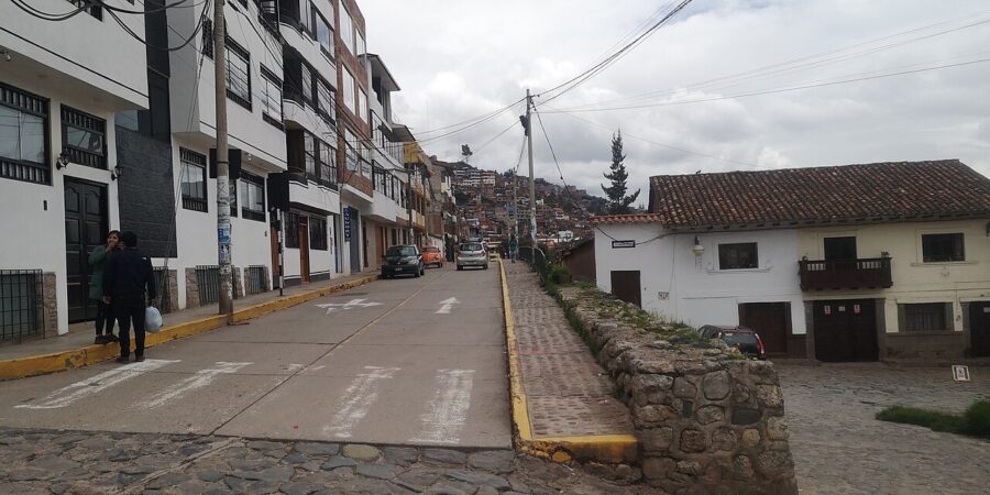 In Lucrepata, Cusco, Peru, an individual walks down the street while holding a bike.