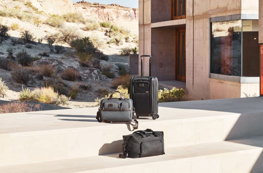 Modern luggage on steps outside a minimalist building against a rugged natural landscape.