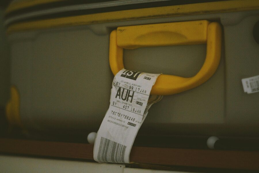 Yellow-handled suitcase with travel tag showing Abu Dhabi airport code (AUH), symbolizing adventure.