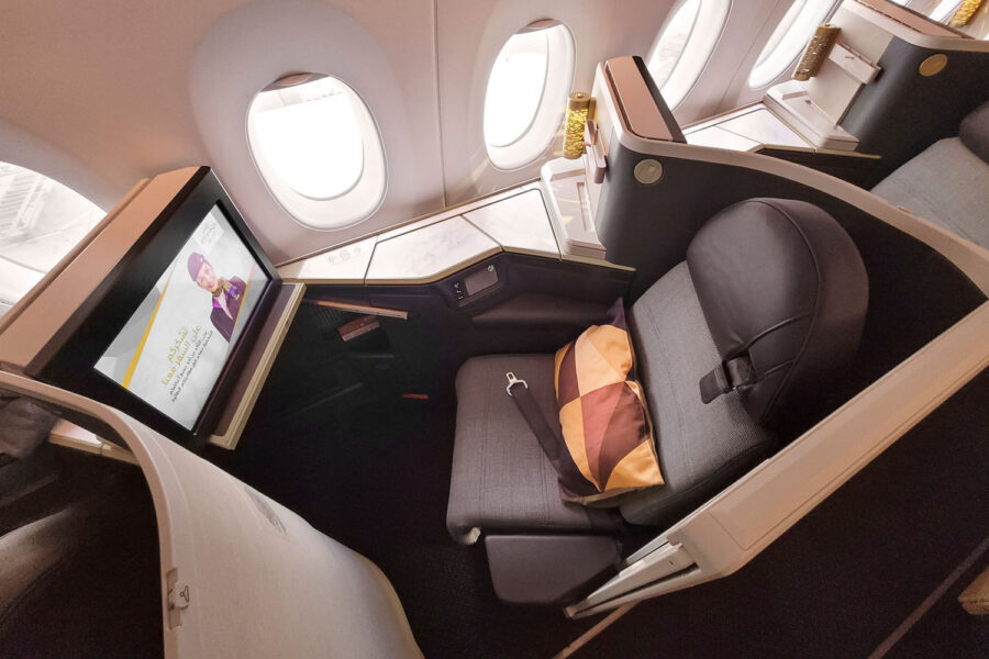 Luxurious business class airplane seat with entertainment screen, modern design, and natural light.