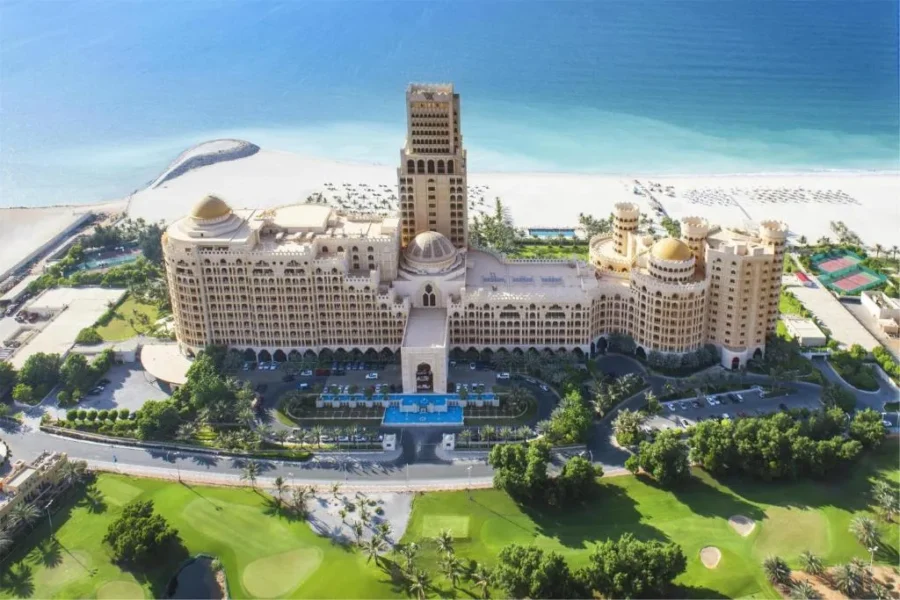 Aerial view of luxury beachfront golf resort with grand palace-style hotel, pool, and private beach.