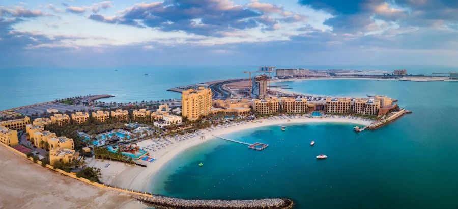 Luxury aerial view of Al Marjan Island beach resort with turquoise lagoon, hotels, pools, and boats.