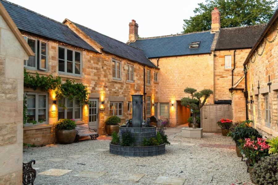 The tranquil courtyard of an old manor house, featuring manicured gardens and classic stonework, part of a luxury Cotswold retreat.