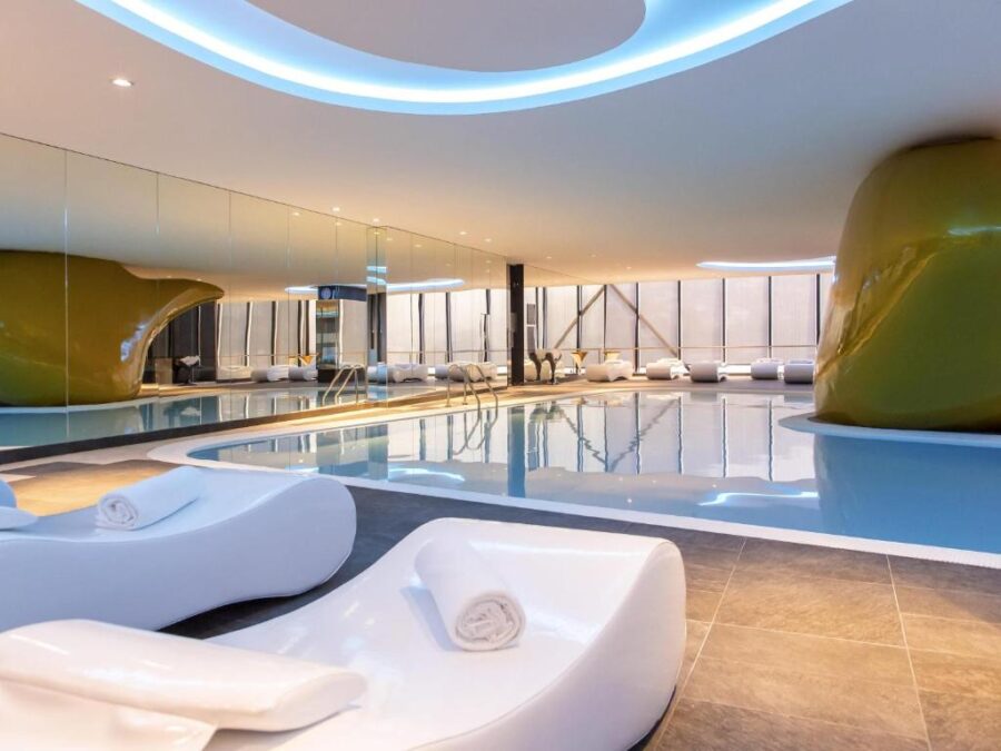 Futuristic luxury indoor hotel pool and spa with sculptural loungers and ambient blue lighting.