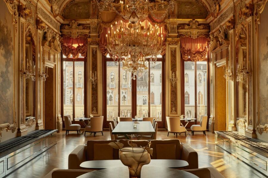 Opulent dining room with gold detailing, chandelier, plush furnishings, and large windows.