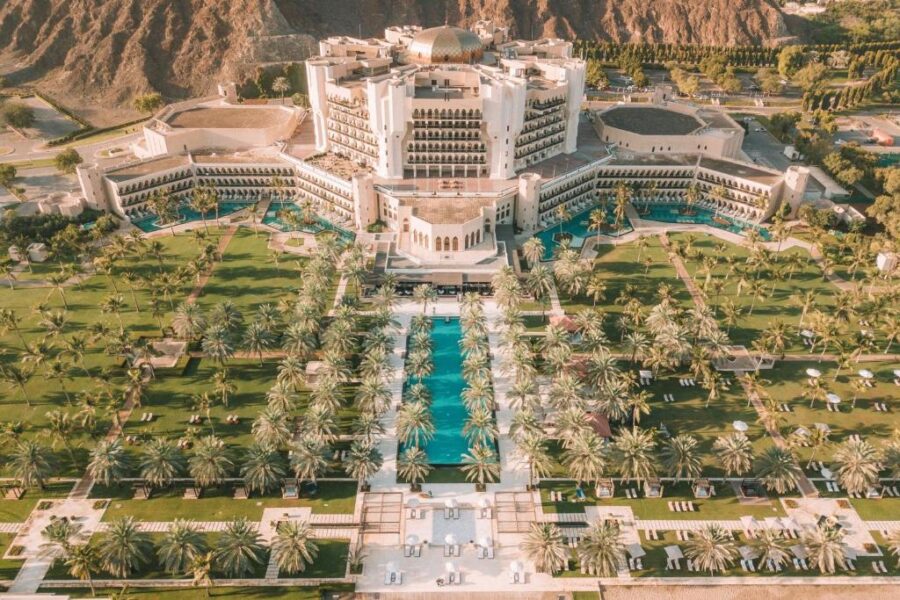 Luxury Oman mountain resort Al Bustan Palace with central turquoise pool, palm trees, and gardens.
