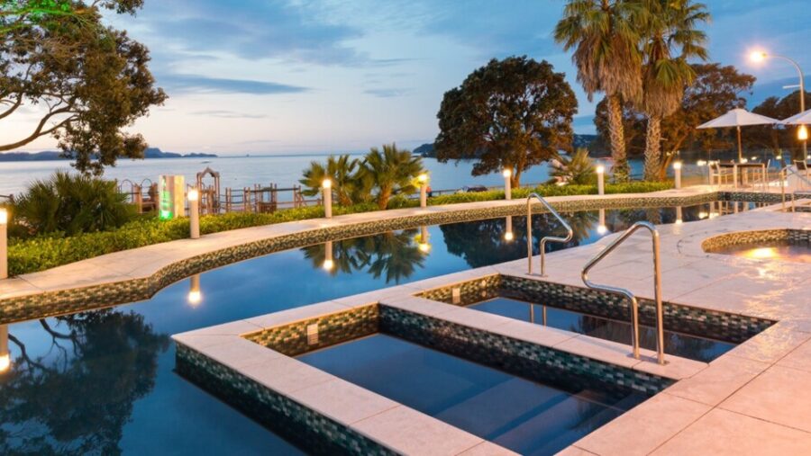 Luxury oceanfront resort infinity pool and hot tubs at dusk overlooking tranquil bay.
