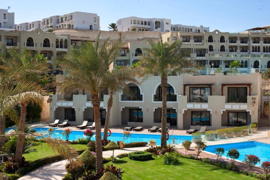 Luxury beachfront resort with palm trees, landscaped gardens, and turquoise swimming pool in Sharm El Sheikh.