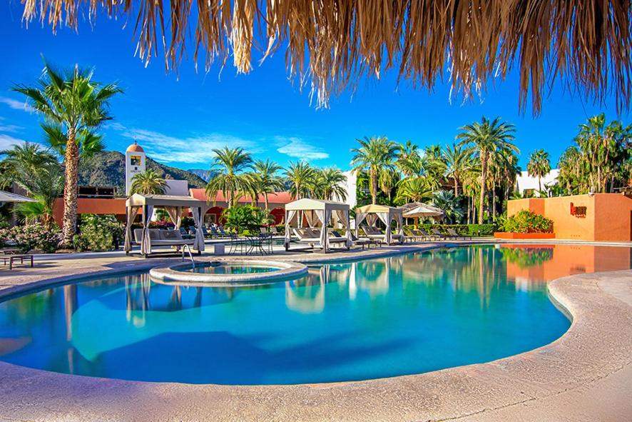 Luxury desert resort pool with cabanas, palm trees, hot tub, and mountain views.