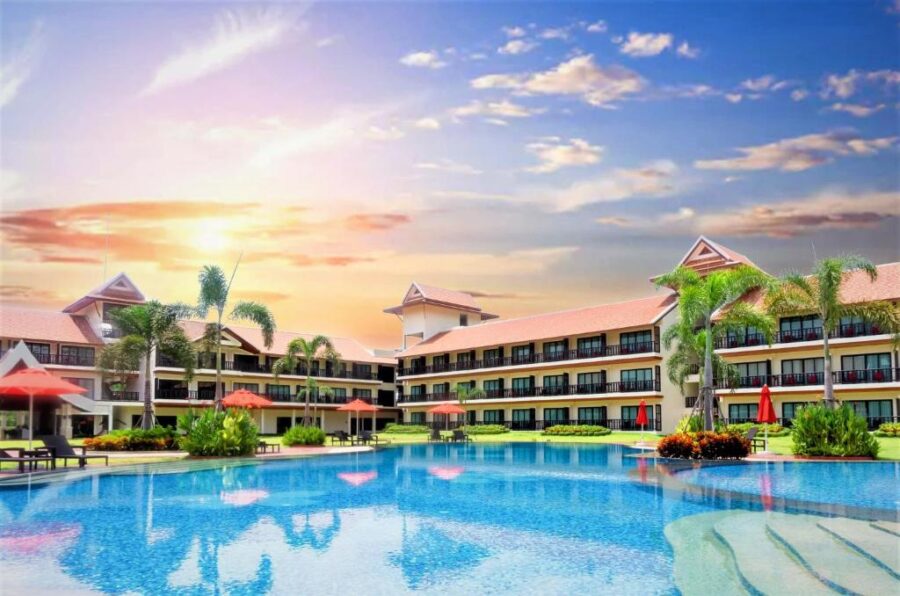 Luxury tropical resort pool at sunset with palm trees, sun loungers, and scenic hotel views.