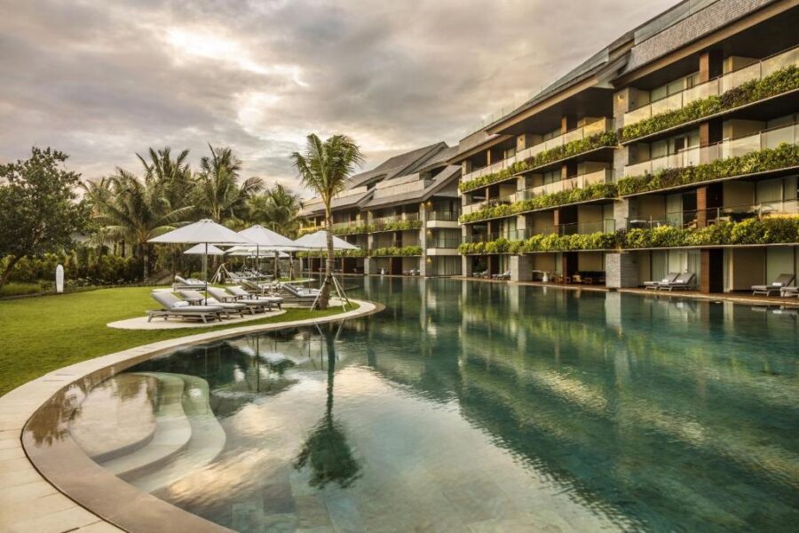 Luxury beachfront resort infinity pool with palm trees, sun loungers, and modern oceanview suites.